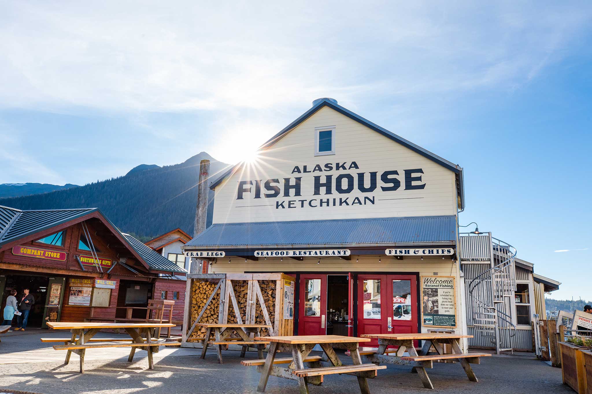 Sunny view of a seafood restaurant in Ketchikan, Alaska, with wooden tables and mountains in the distance.