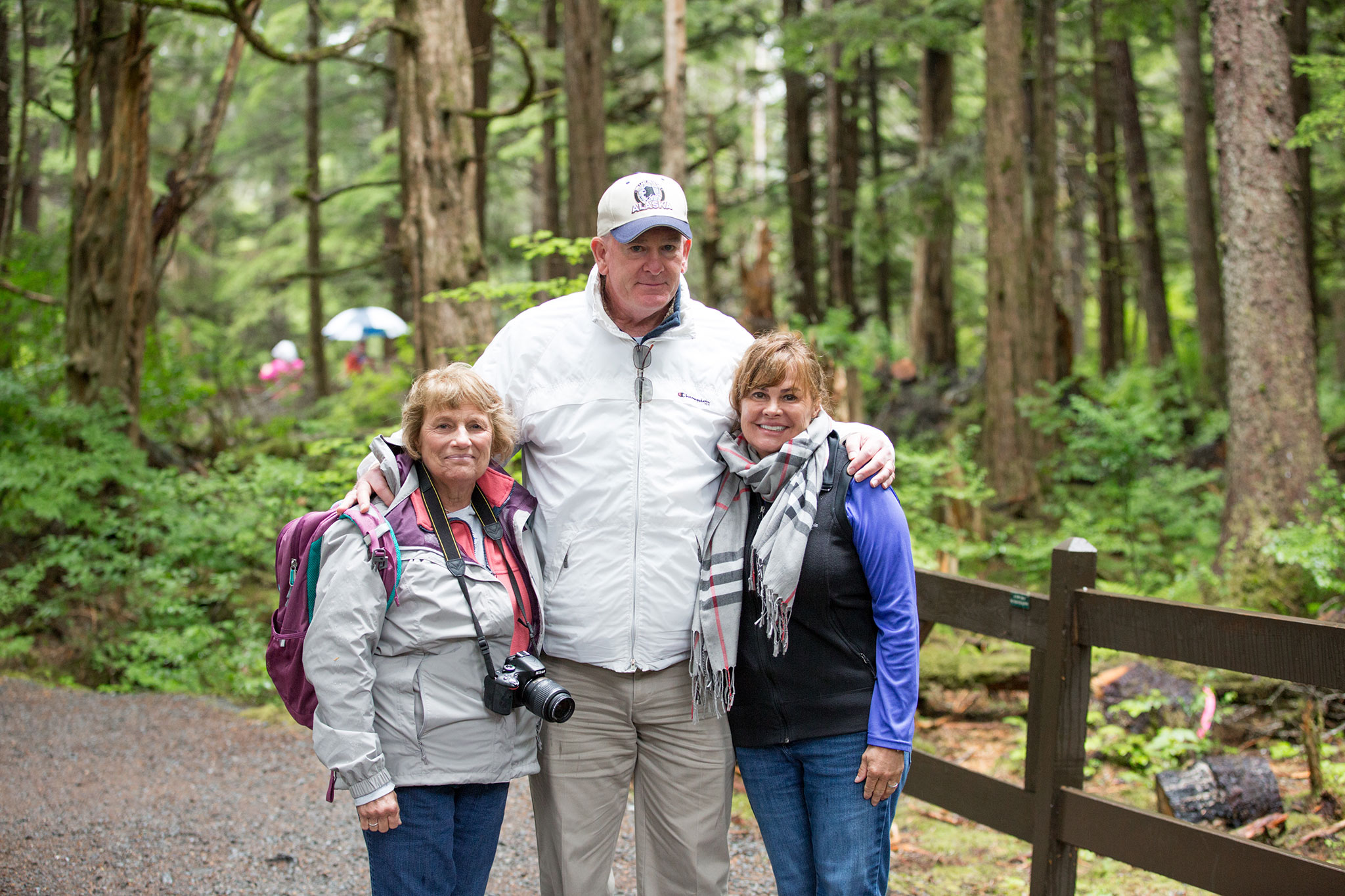 A group photo of two women and one man, all dressed in outdoor gear, standing on a forest trail.