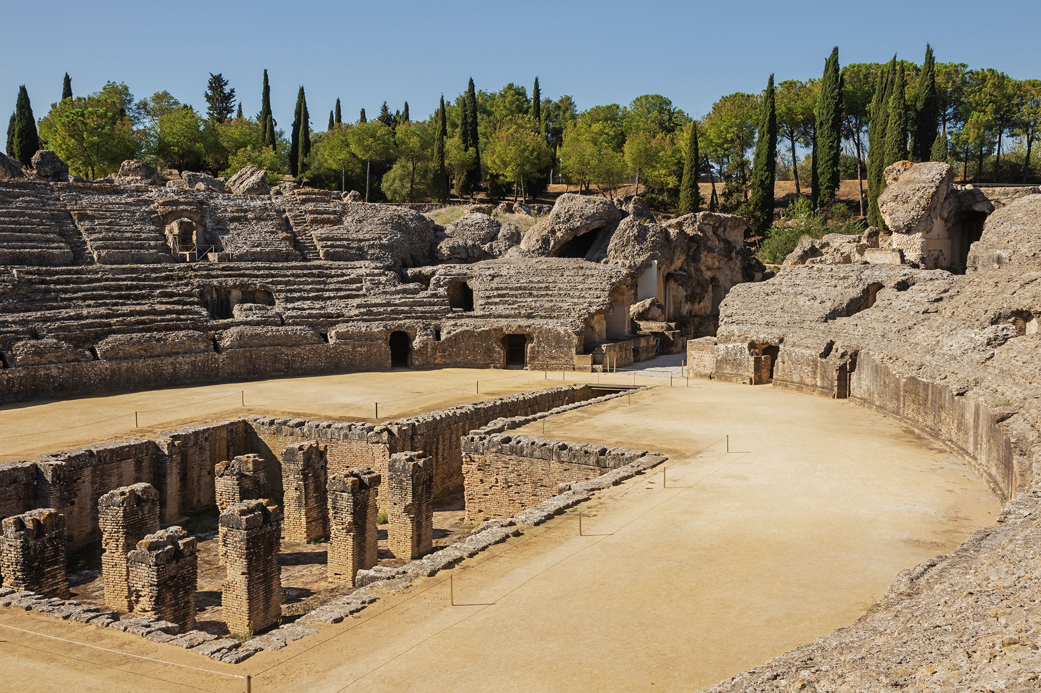 Ancient amphitheater ruins surrounded by cypress trees.