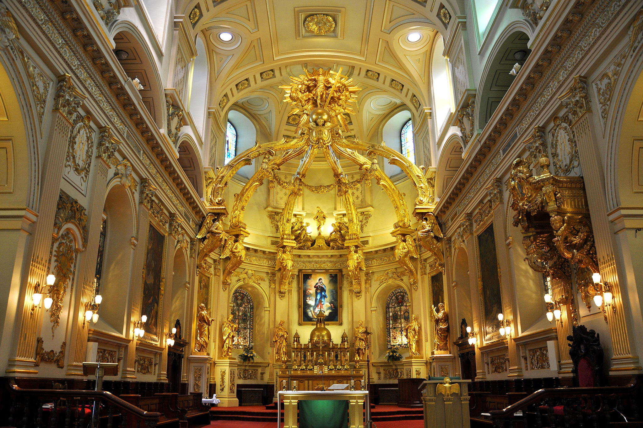 Grand cathedral interior showcasing intricate gold detailing and a central Virgin Mary painting.