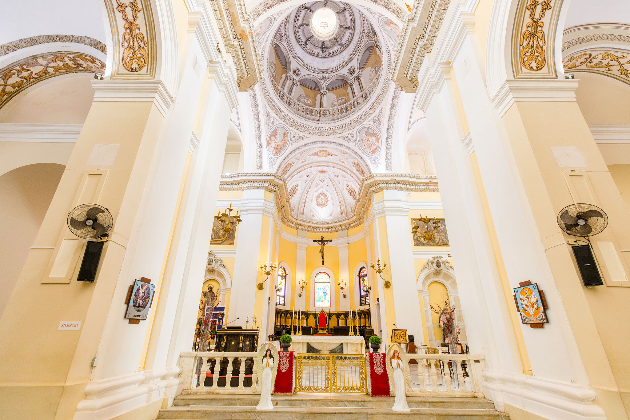 San Juan Bautista Cathedral’s ornate interior with arched ceilings, stained glass windows, a central crucifix and a lavish altar adorned with gold details, chandeliers and statues.