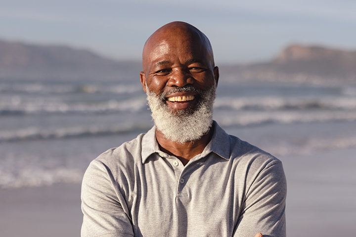 A smiling man standing on the beach with ocean waves in the background