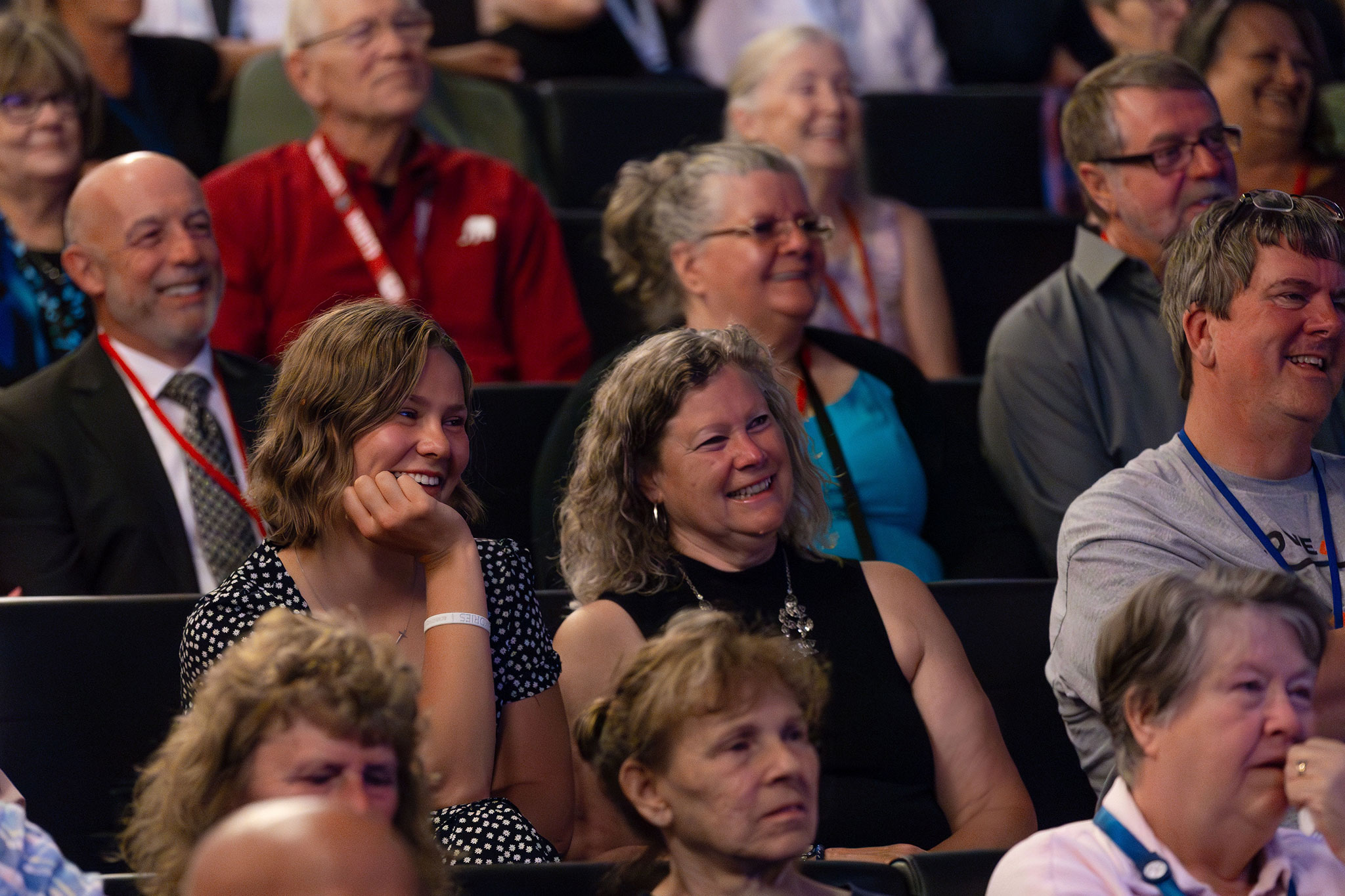A Group of people seated in rows enjoys an event, many smiling and engaged.