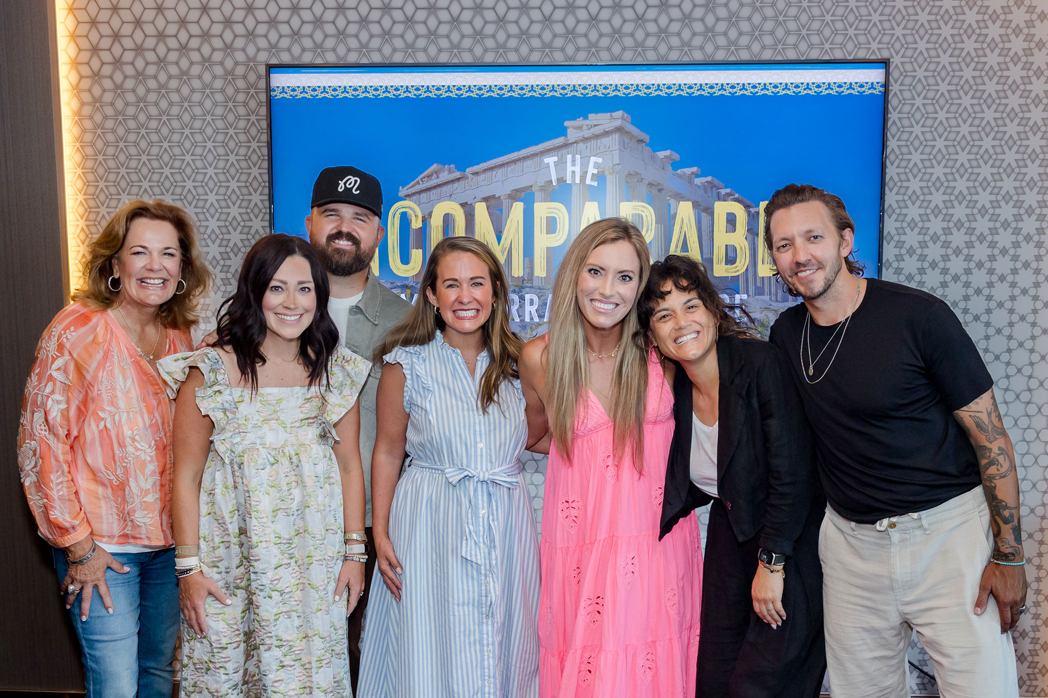 Seven people stand closely, including Levi and Jennie Lusko and Lisa Harper, smiling for a group photo in front of an event display backdrop
