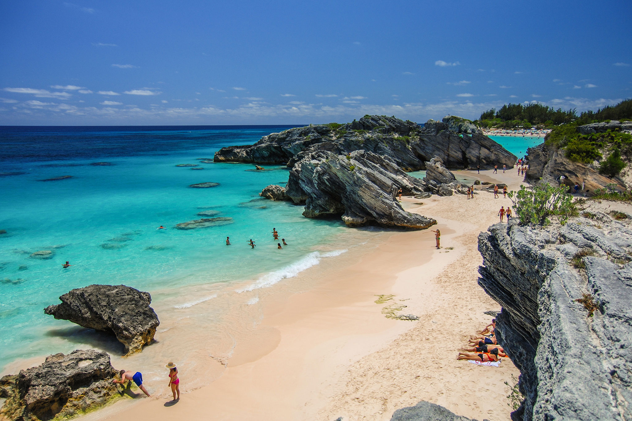 Visitors swimming and relaxing along the pink sand and rocky cliffs at Horseshoe Bay Beach in Bermuda.