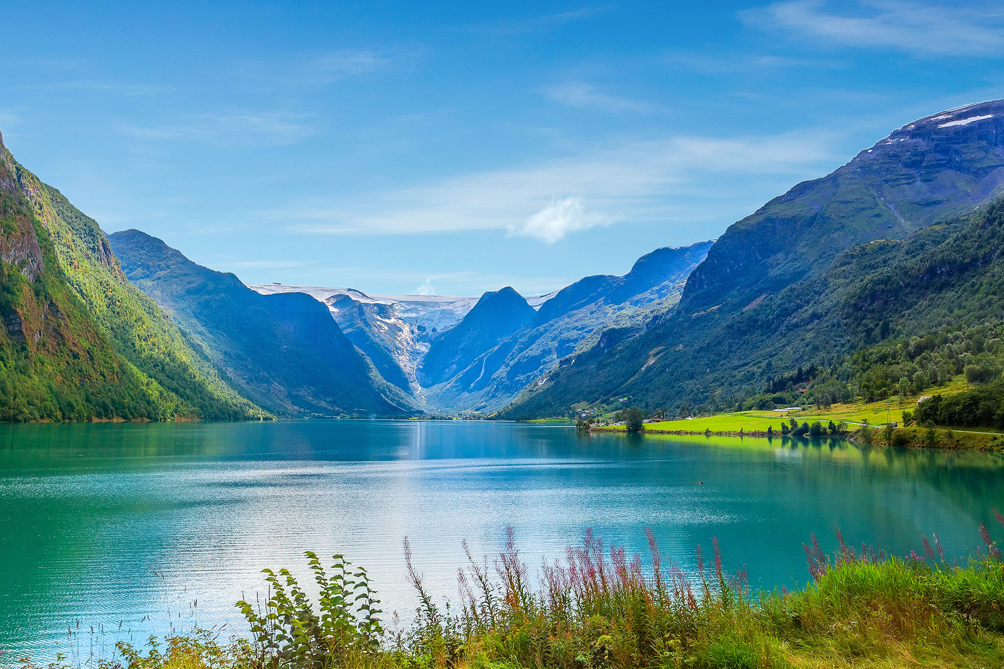 Panoramic view of Nordfjord, Norway, with turquoise waters, steep green mountains, and distant snowcapped peaks.