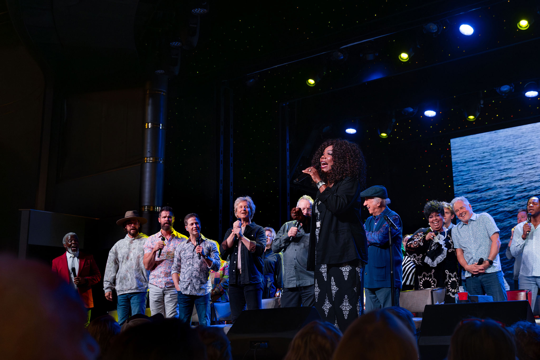 Lynda Randle leads a song onstage alongside members of the Gaither Homecoming group, all singing under bright stage lights.