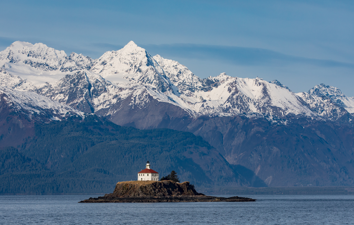 Eldred Rock Lighthouse in Lynn Canal, Alaska, set on a small island with snow-capped mountains in the background.