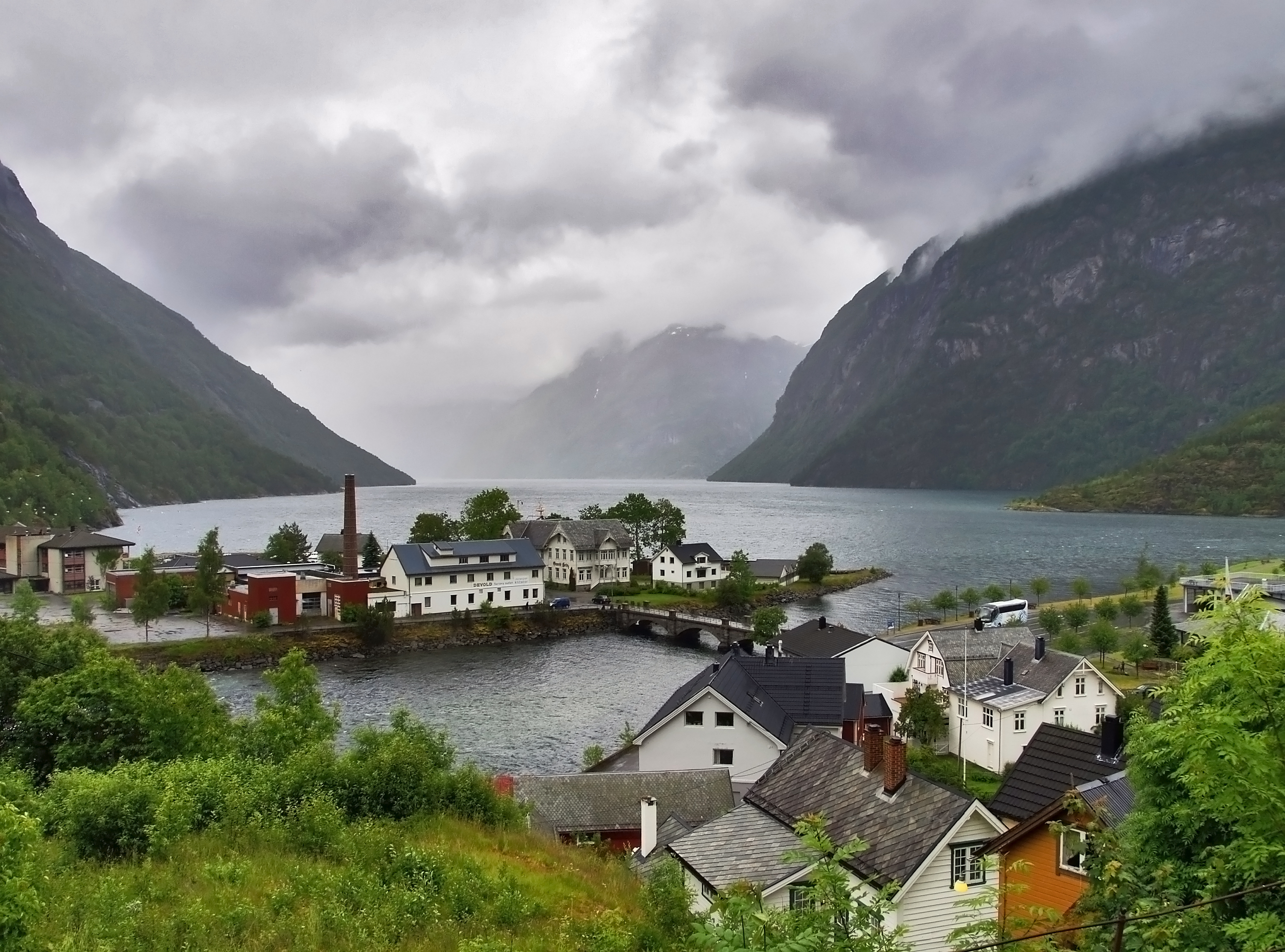 Norwegian fjord village with colorful houses, waterfront buildings, and steep mountains under cloudy skies.