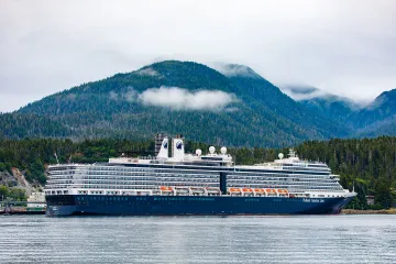 Scenic view of a large cruise ship anchored near a lust forested shortline with foggy mountains in the background.