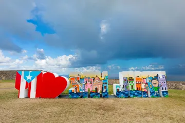 Painted public art display spelling out San Juan, set against a dramatic, cloudy sky.