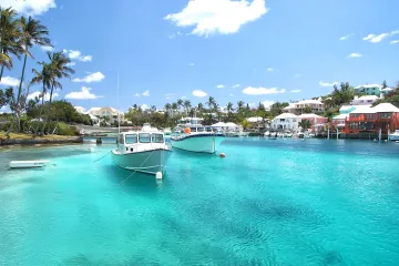 Small boats floating in a bright, tropical bay surrounded by pastel buildings in Bermuda.