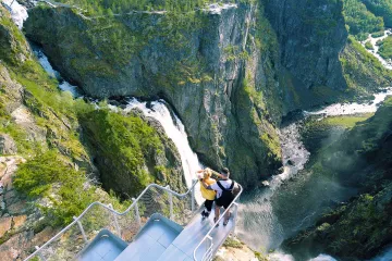 Couple at the Voringsfossen viewpoint overlooking the powerful waterfall cascading through a steep, rocky gorge.