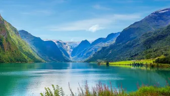 Panoramic view of Nordfjord, Norway, with turquoise waters, steep green mountains, and distant snowcapped peaks.