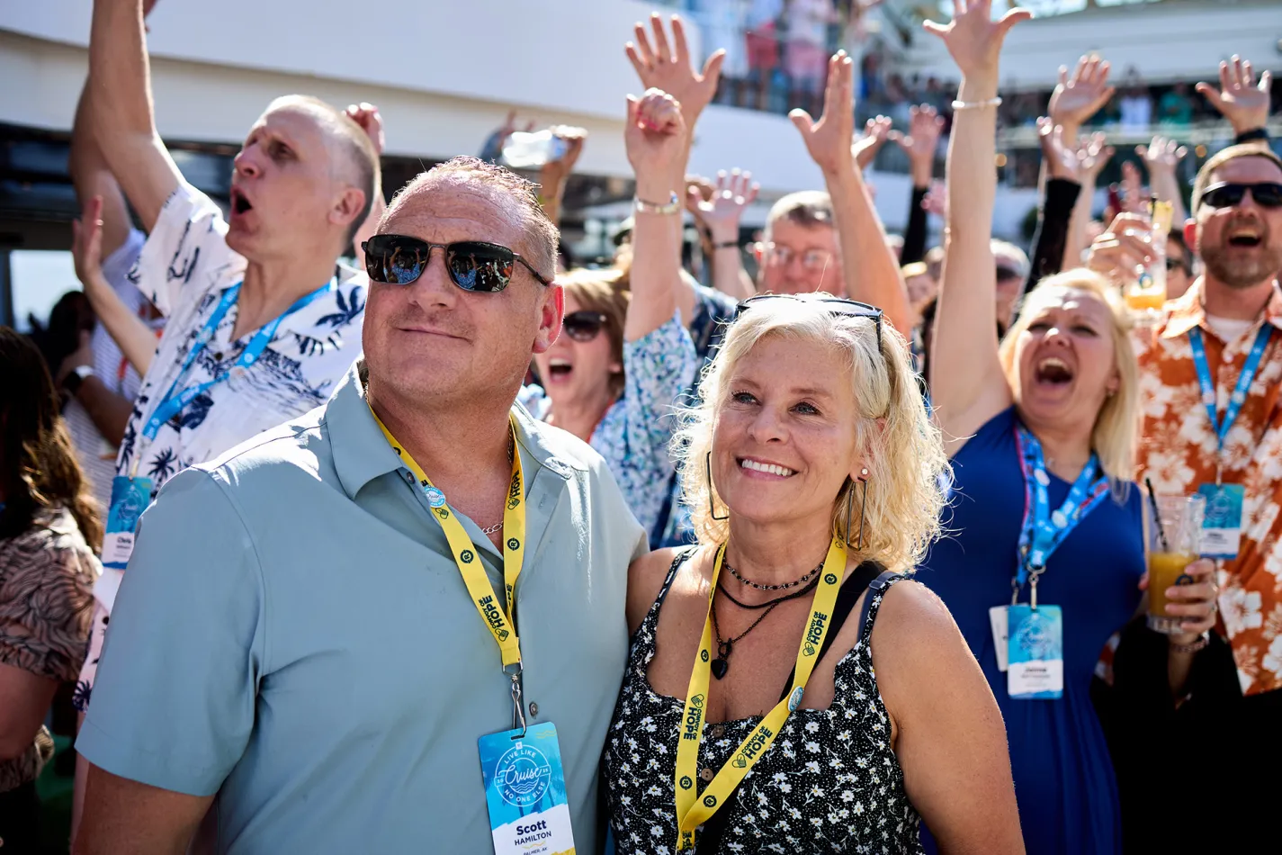Smiling couple with a crowd of people lifting their hands in the background