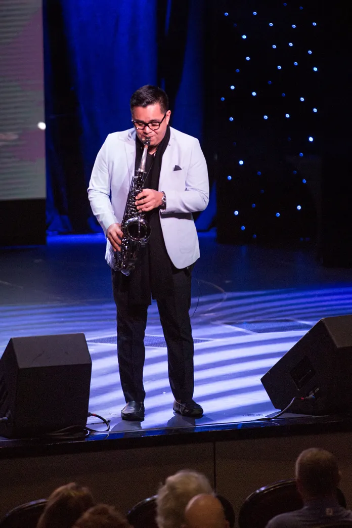 Uriel Vega standing on a stage playing his saxophone 