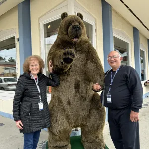 A smiling senior couple standing next to a life size stuffed bear